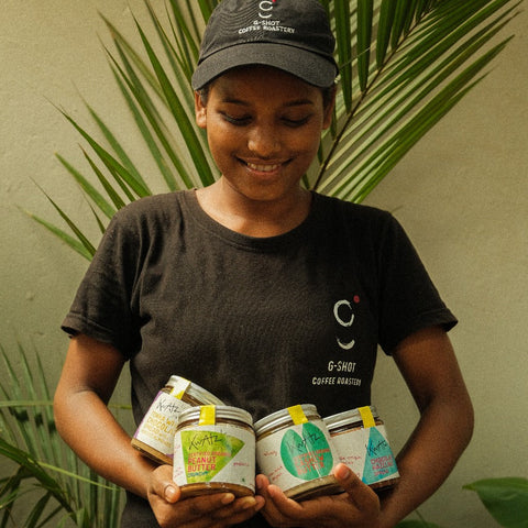 Person holding coffee jars with a plant and framed picture in the background