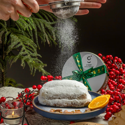 Stollen cake being dusted with powdered sugar, surrounded by festive elements on a dark background.
